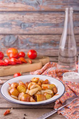 Geleneksel çiftçiler gıda. Havuç, soğan ve tavuk göğsü parçaları ahşap arka plan üzerinde eski metal plaka ile kavrulmuş kırmızı patates. Kırmızı domates ve temiz su bir bardak ile görev yaptı. Leziz yemek.