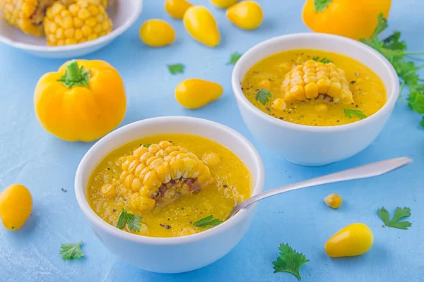 Güzel bir soğuk çorba sarı renk - tatlı Mısır gazpacho, sarı domates ve sarı biber, Mısır ve maydanoz mavi bir arka plan üzerinde beyaz kase bir parçası ile tepesinde. Vejetaryen kavramı.