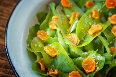 Sebze salatası. Roka, pişmiş dilimlenmiş havuç, zeytinyağında koyu ahşap arka plan üzerinde metal plaka ile sağlıklı yemek. Sağlıklı bir diyet yemek