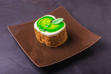 Karanlık bir arka plan üzerinde kahverengi bir plaka üzerinde bir yeşil elma şeklinde kek lezzetli tatlım.