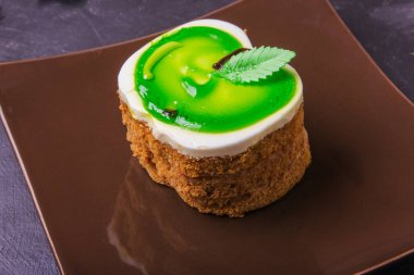 Karanlık bir arka plan üzerinde kahverengi bir plaka üzerinde bir yeşil elma şeklinde kek lezzetli tatlım.