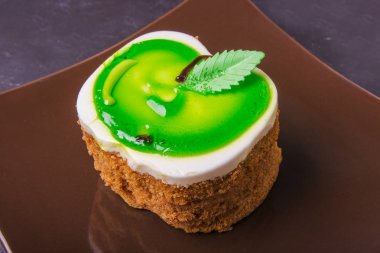 Karanlık bir arka plan üzerinde kahverengi bir plaka üzerinde bir yeşil elma şeklinde kek lezzetli tatlım.