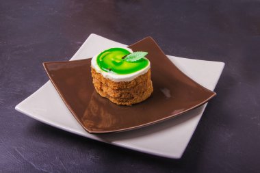 Karanlık bir arka plan üzerinde kahverengi bir plaka üzerinde bir yeşil elma şeklinde kek lezzetli tatlım.