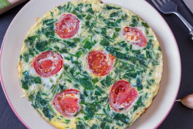 Ispanak frittata, karanlık bir arka plan üzerine bir tabak içinde kiraz domates ile İtalyan omleti. Sağlıklı gıda anlayışı.