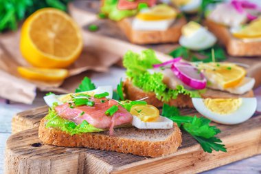 Taze yeşil salata, soğan halkası, yumurta, evde peynir, limon, mikro yeşil ve scallions ahşap masa üzerinde bir çeyrek ile ringa balığı ve ton balığı fileto sandviç.