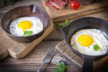 İki küçük kızartma tavada kızarmış yumurta tohumlar, jambon, domates ve maydanoz ile ev yapımı ekmek ile servis edilir. Lezzetli yemekler.