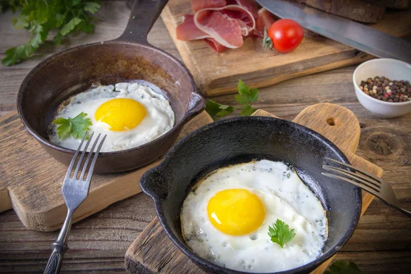 İki küçük kızartma tavada kızarmış yumurta tohumlar, jambon, domates ve maydanoz ile ev yapımı ekmek ile servis edilir. Lezzetli yemekler.