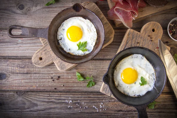İki küçük kızartma tavada kızarmış yumurta tohumlar, jambon, domates ve maydanoz ile ev yapımı ekmek ile servis edilir. Lezzetli yemekler.