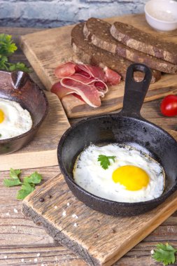 İki küçük kızartma tavada kızarmış yumurta tohumlar, jambon, domates ve maydanoz ile ev yapımı ekmek ile servis edilir. Lezzetli yemekler.