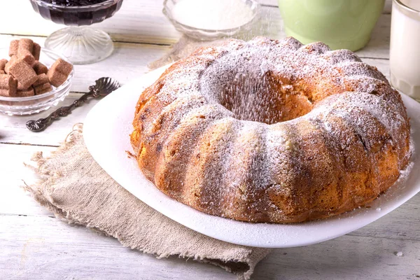 Yuvarlak ahşap bir masa üzerinde beyaz bir tabak üzerinde delik ile ev yapımı pasta tatlı bir bardak süt ile görev yaptı..