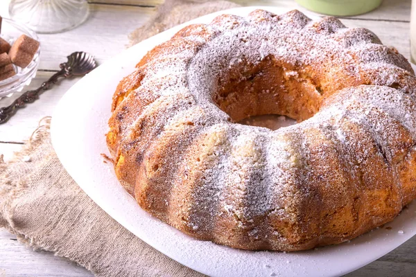 Yuvarlak ahşap bir masa üzerinde beyaz bir tabak üzerinde delik ile ev yapımı pasta tatlı bir bardak süt ile görev yaptı..