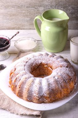 Yuvarlak ahşap bir masa üzerinde beyaz bir tabak üzerinde delik ile ev yapımı pasta tatlı bir bardak süt ile görev yaptı..
