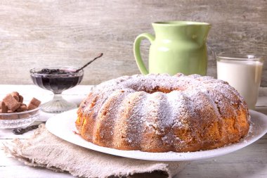 Yuvarlak ahşap bir masa üzerinde beyaz bir tabak üzerinde delik ile ev yapımı pasta tatlı bir bardak süt ile görev yaptı..