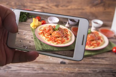 Telefon ile Hands rustik ahşap arka plan üzerinde bir tabakta köfte erişte makarna yemek ile İtalyan mutfağı spagetti resimleri alır