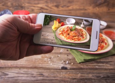 Telefon ile Hands rustik ahşap arka plan üzerinde bir tabakta köfte erişte makarna yemek ile İtalyan mutfağı spagetti resimleri alır