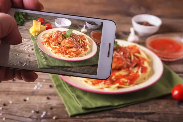 Telefon ile Hands rustik ahşap arka plan üzerinde bir tabakta köfte erişte makarna yemek ile İtalyan mutfağı spagetti resimleri alır