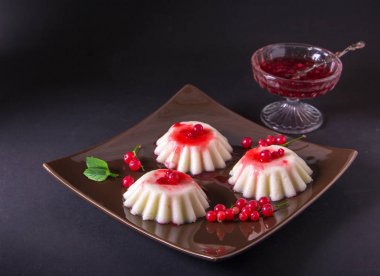 İrmik pudingi bir kahverengi kare plaka Frenk üzümü şurubu ve çilek ile. Karanlık bir arka plan üzerinde