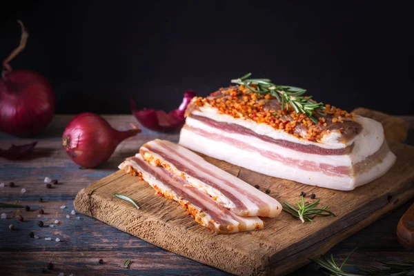 Trozos de tocino salado sobre fondo oscuro. Comida saludable con especias, hierbas está decorado con romero en el escritorio vintage. Grasa, manteca de cerdo, sebo, grasa —  Fotos de Stock