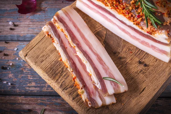 Pedaços de bacon salgado no fundo escuro. Comida saudável com especiarias, ervas é decorado alecrim na mesa vintage. Gordura, banha, sebo, graxa — Fotografia de Stock