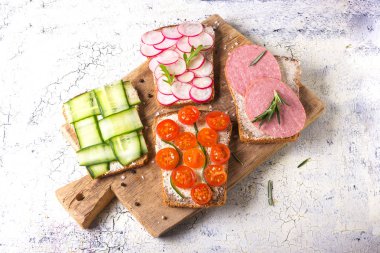 Turp, salatalık, domates ve sosis ile çeşitli sandviç seti, hafif bir arka plan üst görünümünde rustik bir masada arugula ve biberiye ile terbiyeli