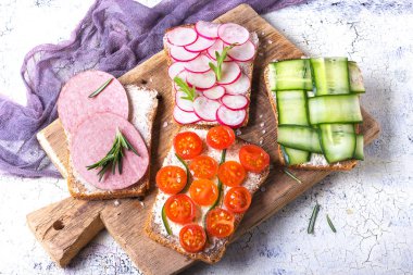 Turp, salatalık, domates ve sosis ile çeşitli sandviç seti, hafif bir arka plan üst görünümünde rustik bir masada arugula ve biberiye ile terbiyeli