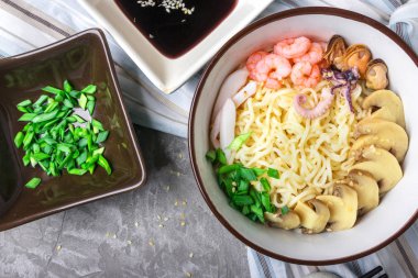 Deniz ürünleri ile Asya buğday erişte, mantar turşusu ve taze soğan, gri bir arka plan üzerinde bir kase susam serpilir. Asya tarzı, Japon yemekleri