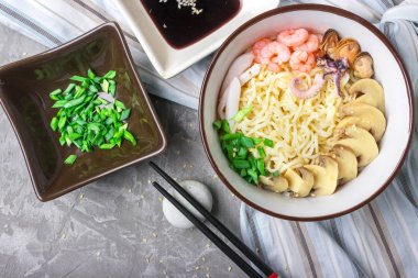 Deniz ürünleri ile Asya buğday erişte, mantar turşusu ve taze soğan, gri bir arka plan üzerinde bir kase susam serpilir. Asya tarzı, Japon yemekleri