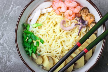 Deniz ürünleri ile Asya buğday erişte, mantar turşusu ve taze soğan, gri bir arka plan üzerinde bir kase susam serpilir. Asya tarzı, Japon yemekleri