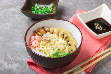 Deniz ürünleri ile Asya buğday erişte, mantar turşusu ve taze soğan, gri bir arka plan üzerinde bir kase susam serpilir. Asya tarzı, Japon yemekleri