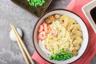 Deniz ürünleri ile Asya buğday erişte, mantar turşusu ve taze soğan, gri bir arka plan üzerinde bir kase susam serpilir. Asya tarzı, Japon yemekleri