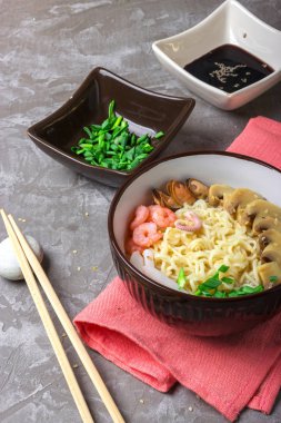 Deniz ürünleri ile Asya buğday erişte, mantar turşusu ve taze soğan, gri bir arka plan üzerinde bir kase susam serpilir. Asya tarzı, Japon yemekleri