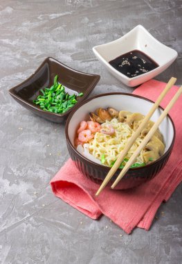 Deniz ürünleri ile Asya buğday erişte, mantar turşusu ve taze soğan, gri bir arka plan üzerinde bir kase susam serpilir. Asya tarzı, Japon yemekleri