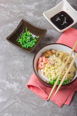 Deniz ürünleri ile Asya buğday erişte, mantar turşusu ve taze soğan, gri bir arka plan üzerinde bir kase susam serpilir. Asya tarzı, Japon yemekleri