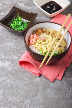 Deniz ürünleri ile Asya buğday erişte, mantar turşusu ve taze soğan, gri bir arka plan üzerinde bir kase susam serpilir. Asya tarzı, Japon yemekleri