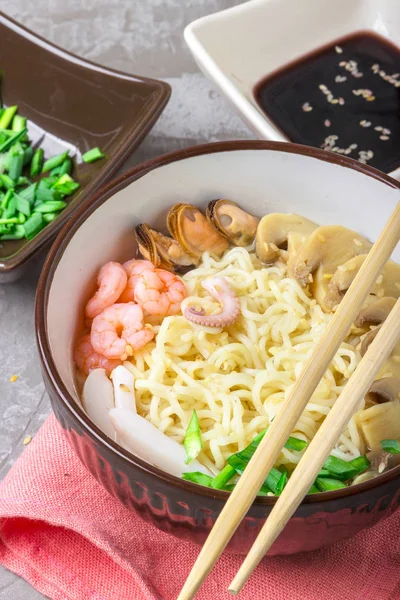 Deniz ürünleri ile Asya buğday erişte, mantar turşusu ve taze soğan, gri bir arka plan üzerinde bir kase susam serpilir. Asya tarzı, Japon yemekleri