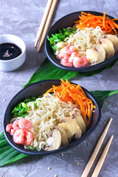 Asian wheat noodles with shrimps, pickled mushrooms, pickled carrots and a scallions in a black plate on green tropical leaves. Asian style, Japanese food'