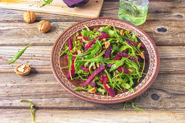 Arugula ile Bahar detoks salata salatası ve ceviz çekirdeği ve kavrulmuş susam ile haşlanmış pancar, ahşap bir arka plan üzerinde rustik seramik plaka zeytinyağı ile dökülür, üst görünümü