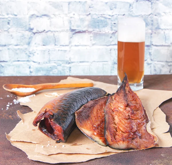 Gerookte makreelfilets op ambachtelijk papier met een glas bier op een rustieke roestige metalen tafel — Stockfoto