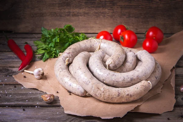 Raw fresh white sausages on a craft paper with vegetables. Weisswurst in a heap. Traditional Bavarian or Munich white sausage made from sliced veal and pork bacon. Oktoberfest concept