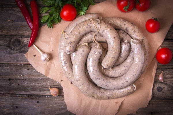 Raw fresh white sausages on a craft paper with vegetables. Weisswurst in a heap. Traditional Bavarian or Munich white sausage made from sliced veal and pork bacon. Oktoberfest concept