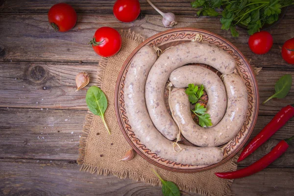 Raw fresh white sausages on a plate with vegetables. Weisswurst in a heap. Traditional Bavarian or Munich white sausage made from sliced veal and pork bacon. Oktoberfest concept