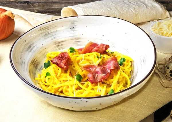 Domuz pastırması, yeşil yaprakları ve parmesan ile kabak noodle. Beyaz kumaş arka planda parmesan ile beyaz plaka üzerinde makarna Carbonara.