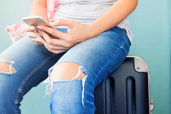 Akıllı telefon, kullanarak seyahat telefon kullanarak kadının ellerini kapatın ve bagaj bavul üzerinde oturan seyahat kavramı