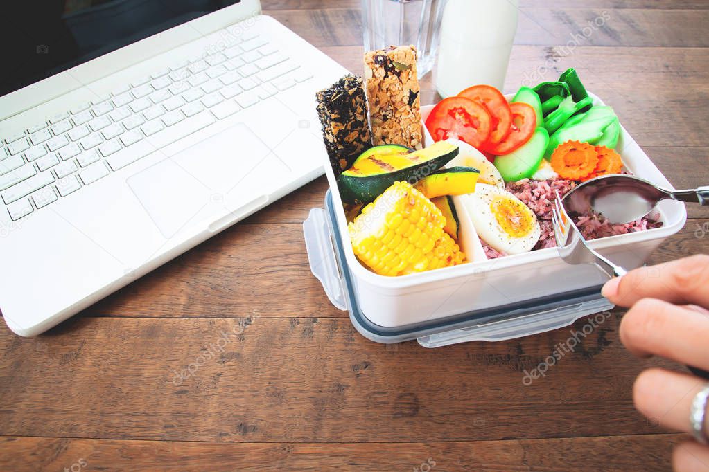 Healthy lunch box with rice berry, boiled eggs, carrot, tomatoes, corns, pumpkin and cereal bars on workspace desk, Food and Health