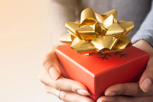 Close up red gift box with gold colour ribbon on woman hands