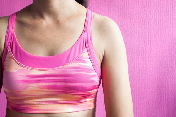 Healthy woman in pink sport bra on pink background, Breast cancer awareness