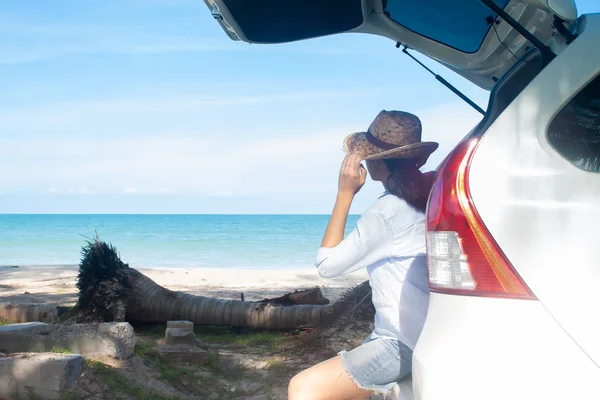 Happy woman in light blue casual shirt and short jeans sitting on car looking to the ocean, Holiday concept