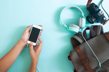 Kadın el ile cep telefonu kullanarak seyahat sırt çantası ve kamera. Renk arka plan üzerinde üstten görünüm