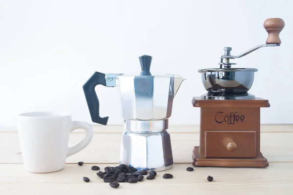 White cup, coffee pot, coffee grinder and coffee beans on wooden table