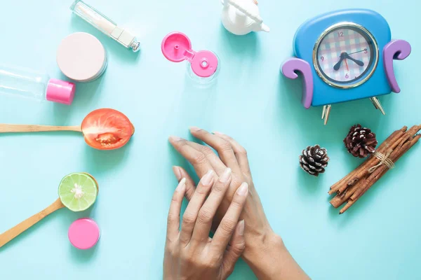 Woman's hands applying lotion on skin. Cosmetic containers and natural ingredient on pastel background